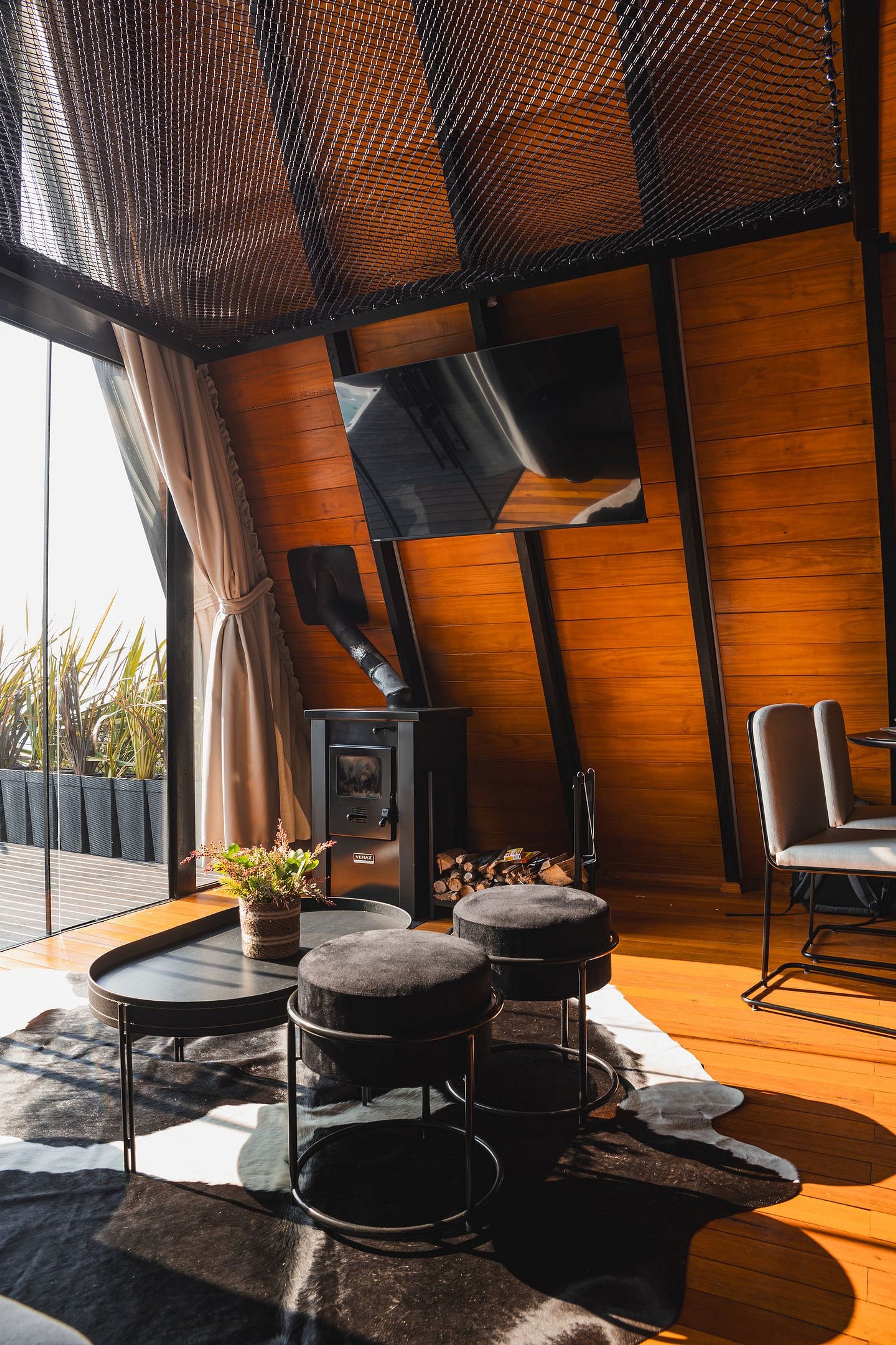 A modern interior with a wooden ceiling, a fireplace, a dining area with a table and chairs, and a large window with curtains.