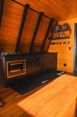 Cocina compacta con horno empotrado, encimera negra y paredes de madera.