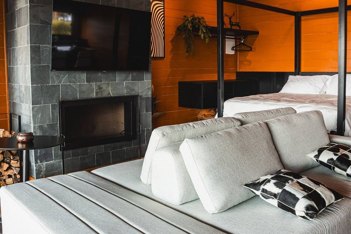 A modern bedroom with a stone fireplace, a bed, and a grey sofa.