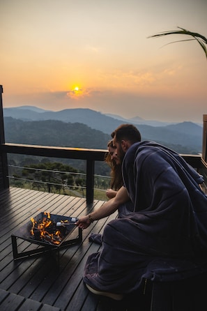 Una pareja en una cubierta de madera con vistas a un paisaje montañoso al atardecer.