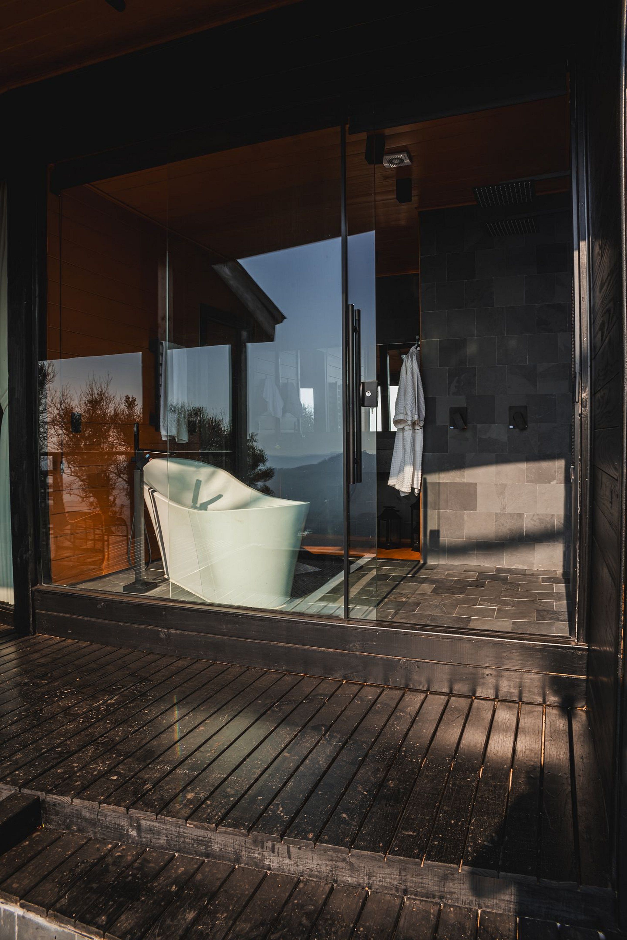 A modern bathroom with a glass shower enclosure, a wooden floor, and a visible towel rack.