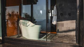A modern bathroom with a glass shower enclosure, a wooden floor, and a visible towel rack.