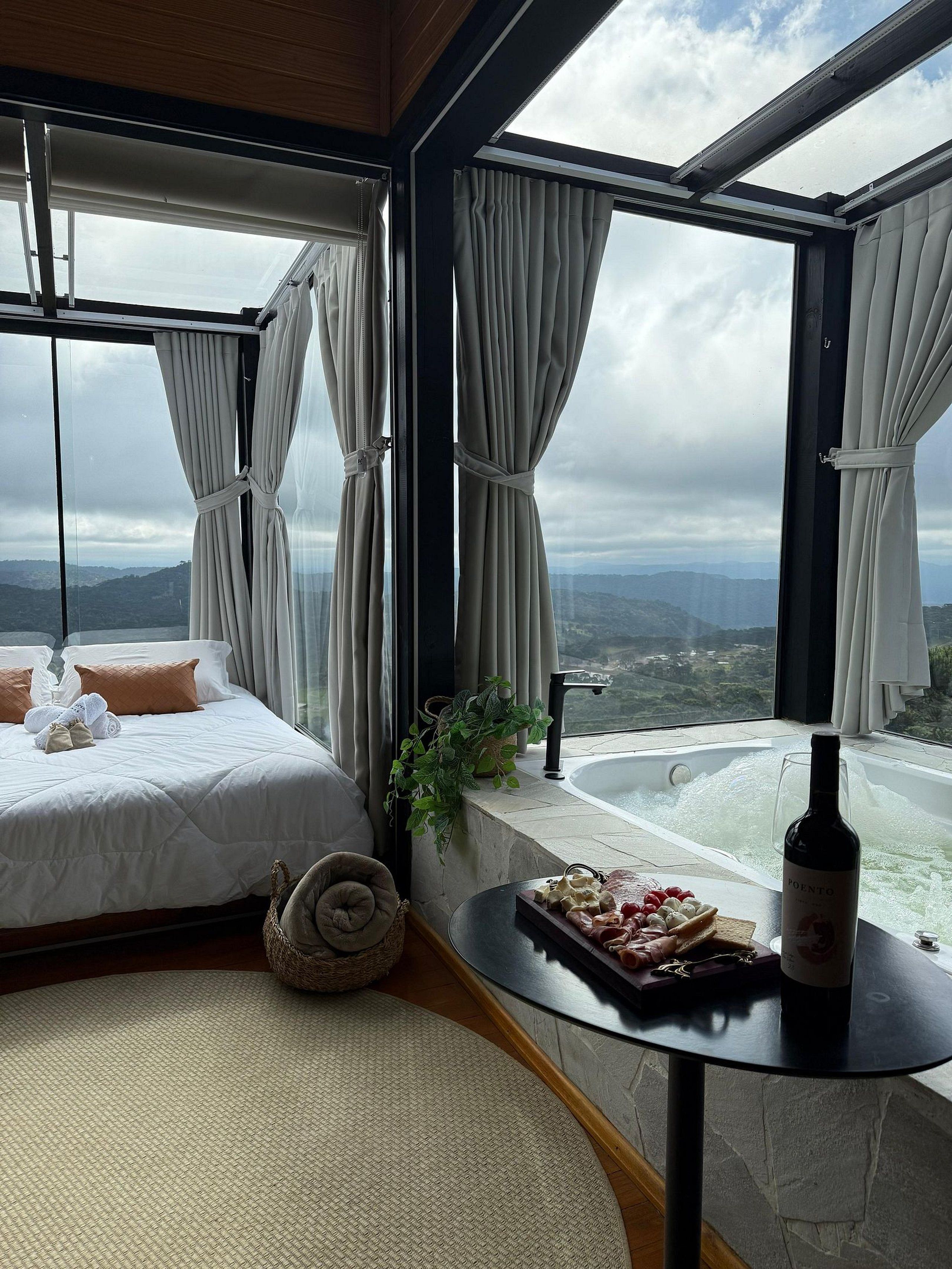 Ein Schlafzimmer mit Bett, Blick auf die Berge, einer Badewanne und einer Weinflasche auf einem Tisch.