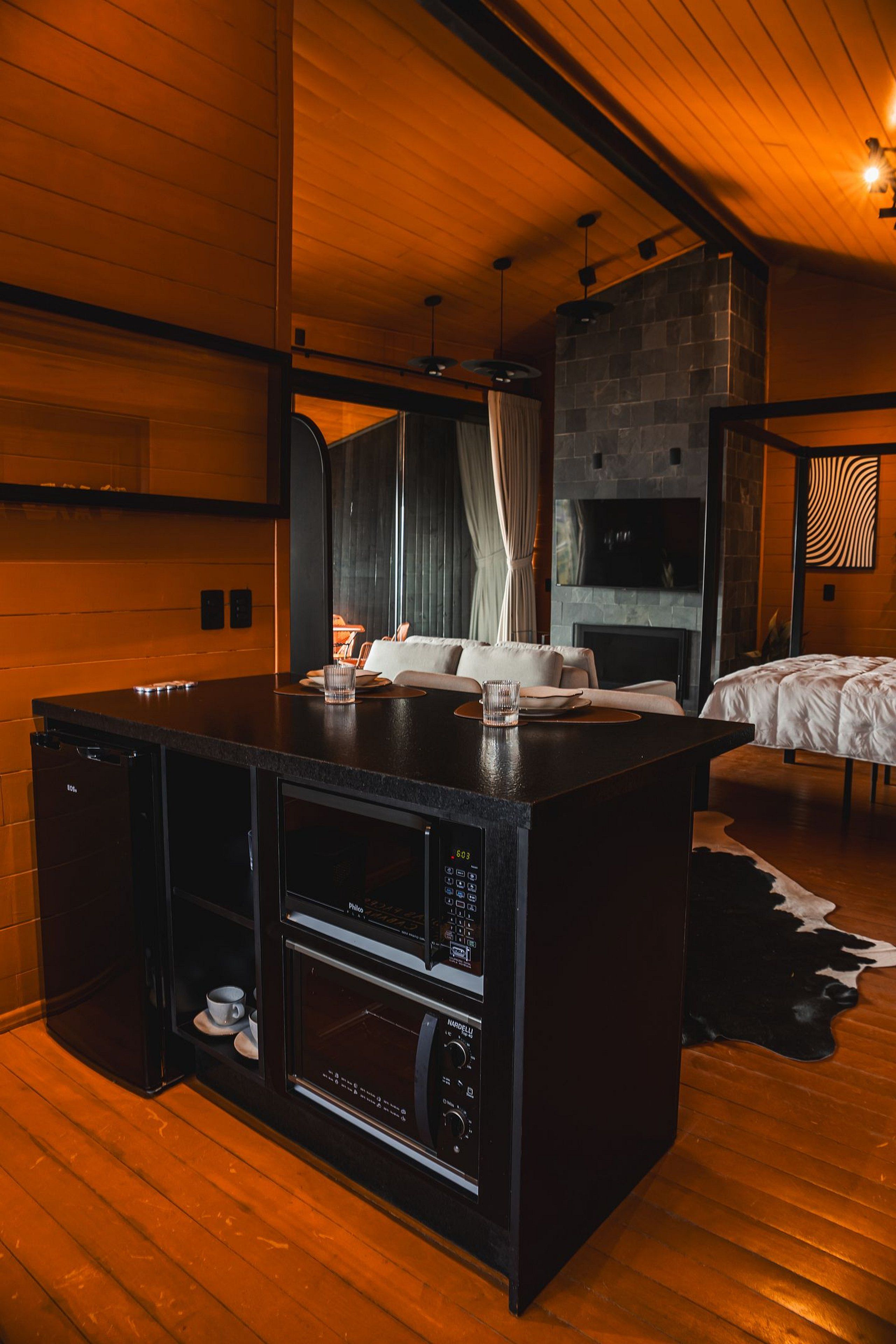 Una habitación moderna con techo de madera, chimenea de piedra, zona de comedor con mesa negra y cama con cubrecama blanco.