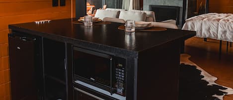 Una habitación moderna con techo de madera, chimenea de piedra, zona de comedor con mesa negra y cama con cubrecama blanco.
