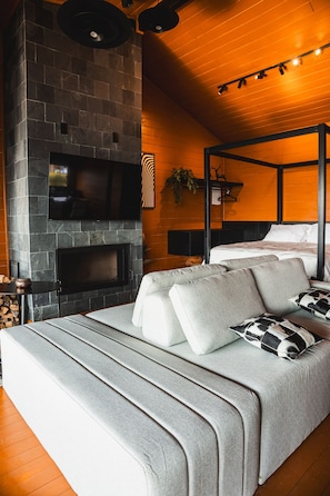 Un dormitorio moderno con chimenea de piedra, una cama y un sofá gris.