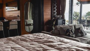 A bedroom with a large bed, a desk, a chair, a mirror, and a view of the outdoors.