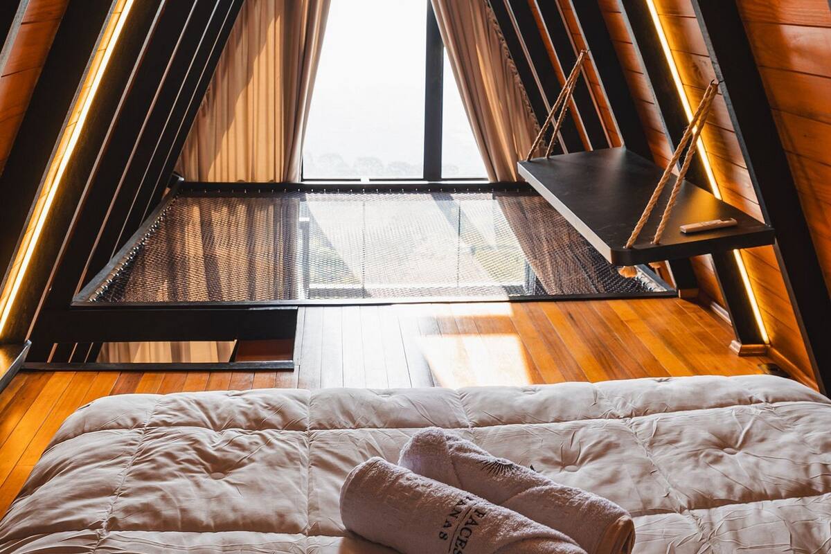 A bedroom with a sloped ceiling, a bed with a white duvet, and a window with a view of the city.