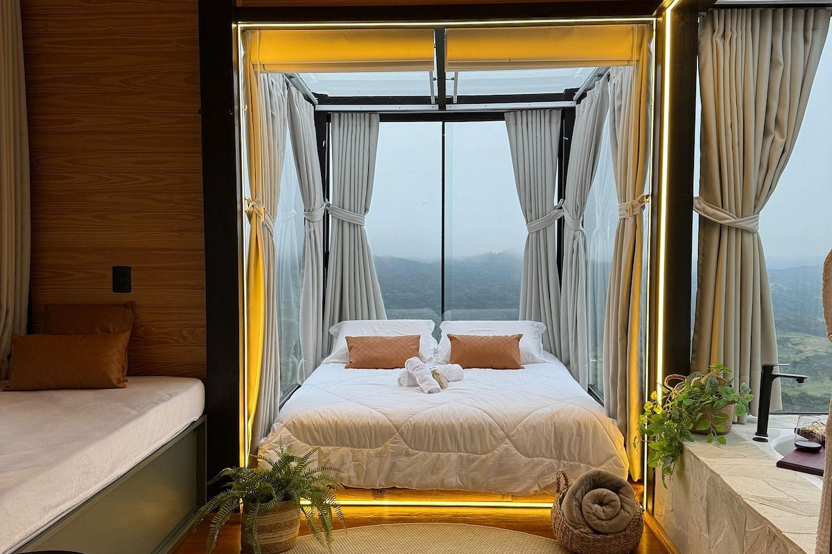 Ein modernes Schlafzimmer mit einem großen Bett, Blick auf die Berge und einer Holzbalkendecke.