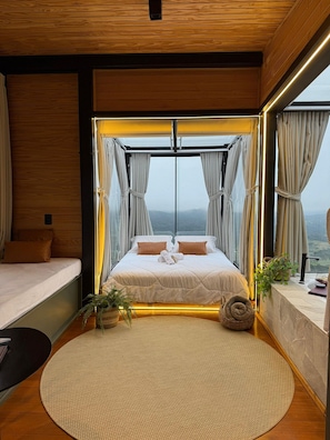Ein modernes Schlafzimmer mit einem großen Bett, Blick auf die Berge und einer Holzbalkendecke.