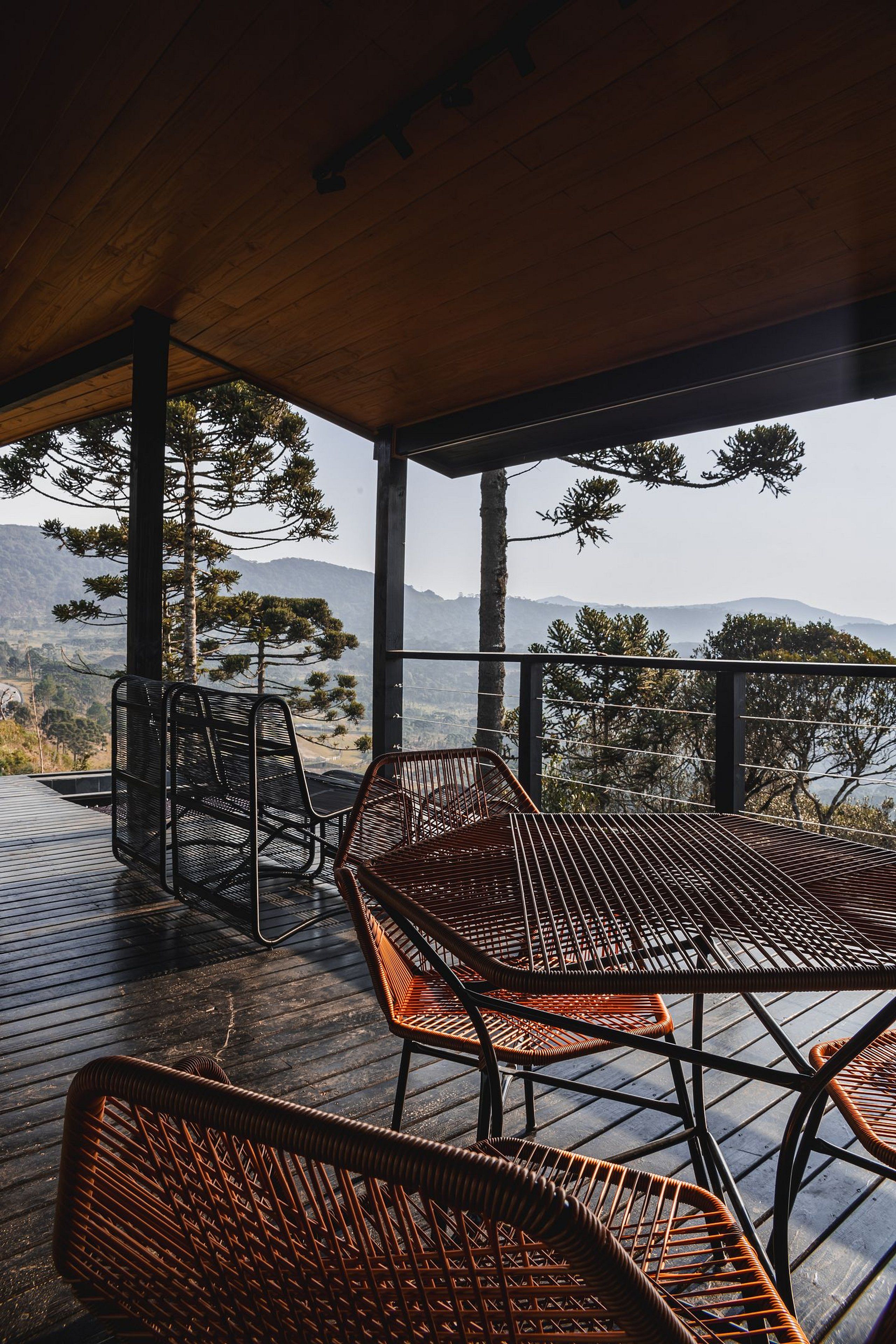 A covered outdoor seating area with metal and wicker chairs, overlooking a mountainous landscape.