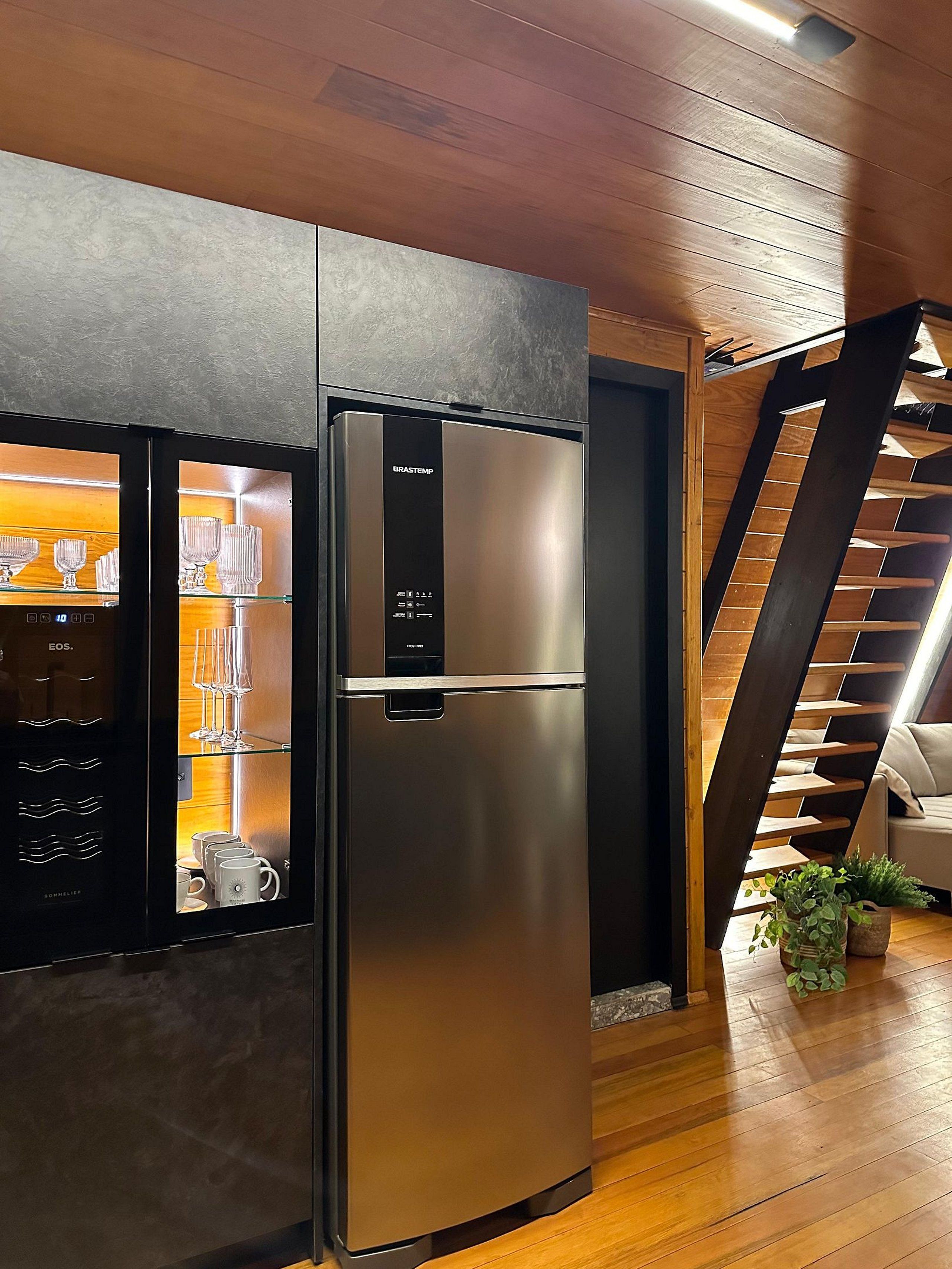 Une cuisine moderne dotée d’un réfrigérateur en acier inoxydable, d’un plancher en bois et d’un escalier menant à un niveau supérieur.