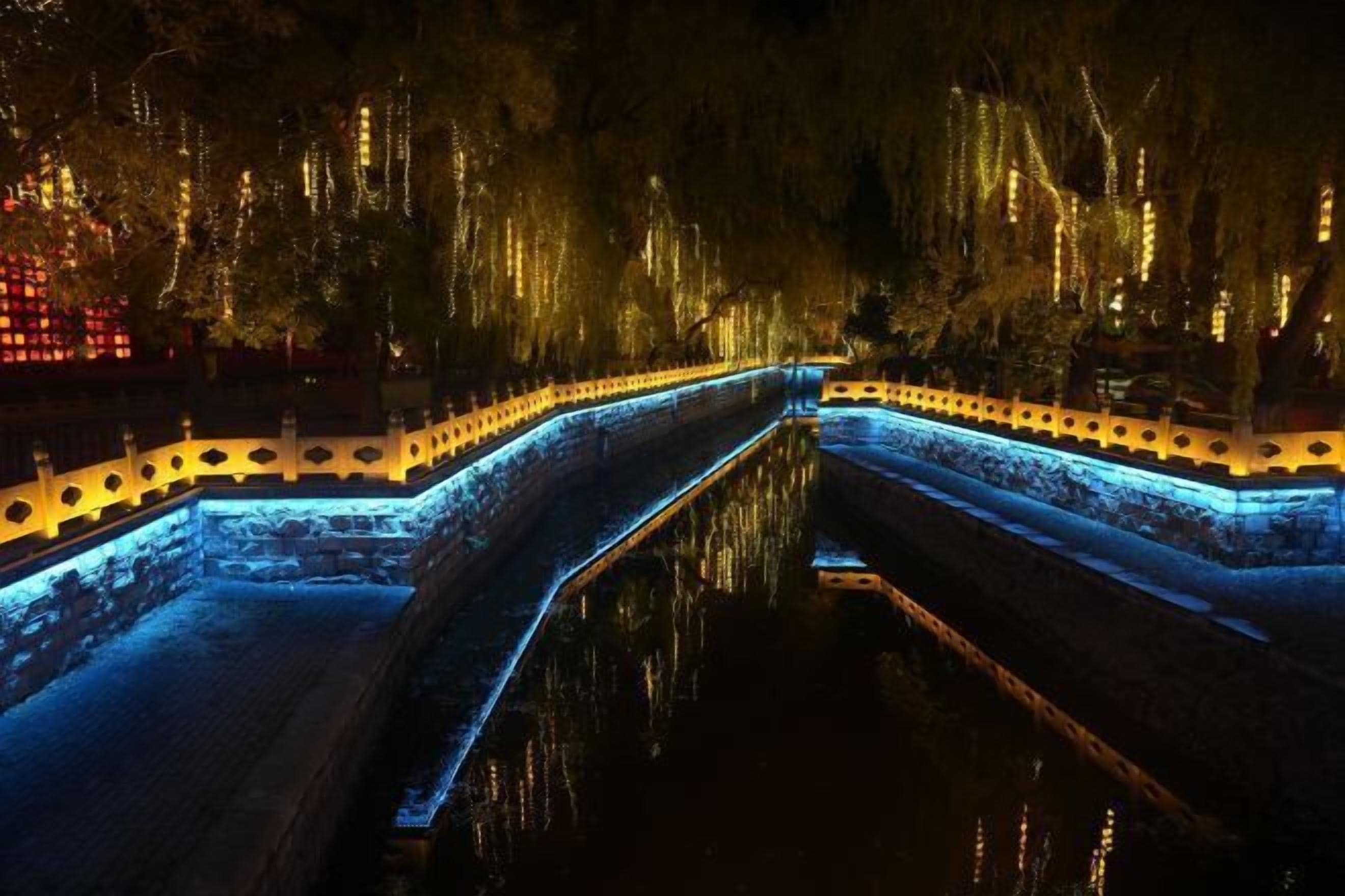 Une vue nocturne d’un canal, avec des passerelles illuminées et un mur de pierre.