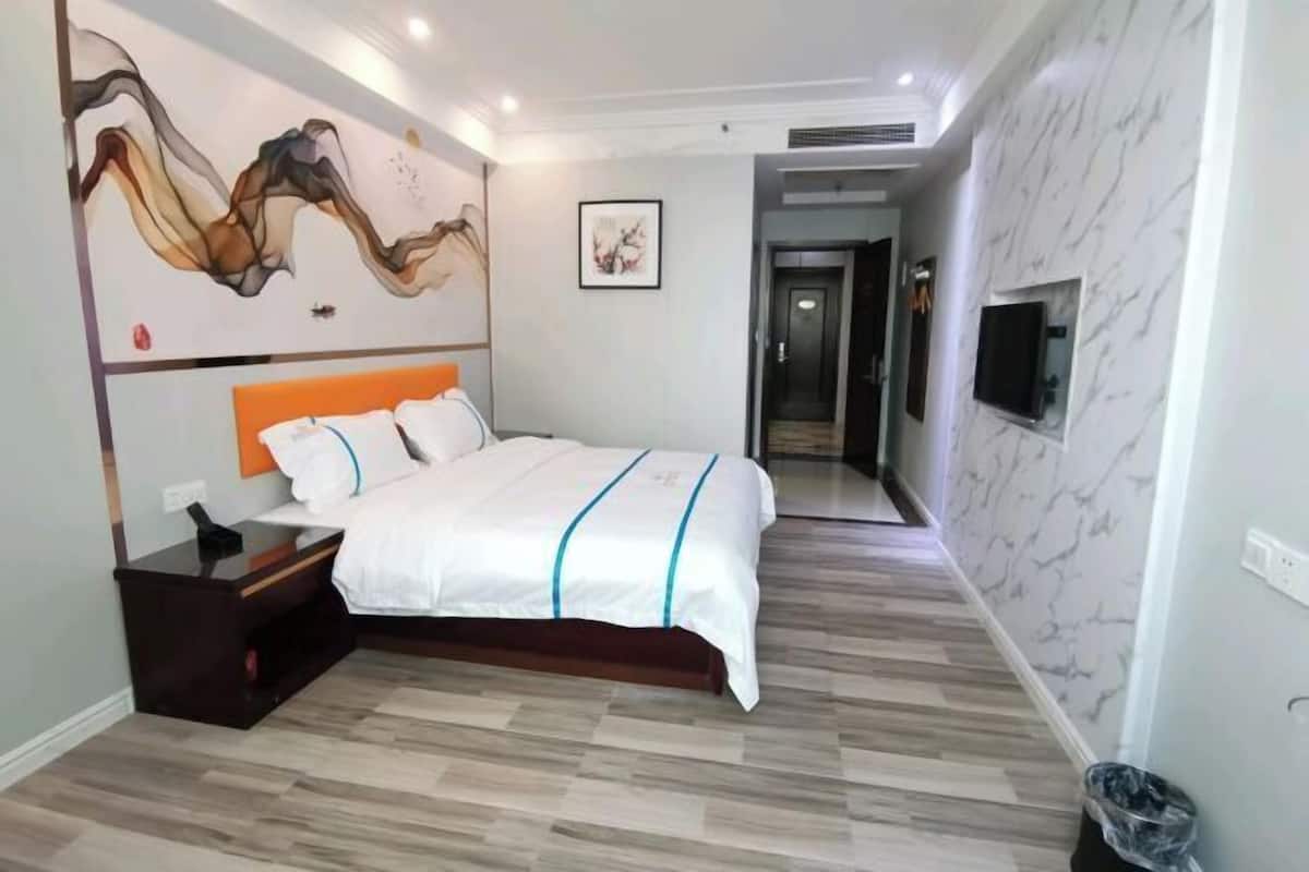 A modern hotel room with a large bed, a nightstand, a wall-mounted TV, and a hallway leading to another room.