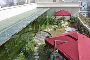 A rooftop garden with a glass wall, red umbrellas, and stepping stones. - Haopai Hotel (Shantou)