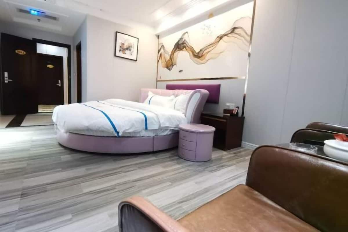 A modern hotel room with a circular bed, a small round table, and a brown leather chair.