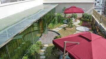 A rooftop garden with a glass wall, red umbrellas, and a circular seating area.