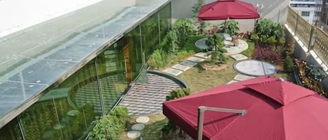 Un jardín en la azotea con pared de cristal, sombrillas rojas y una zona de estar circular.