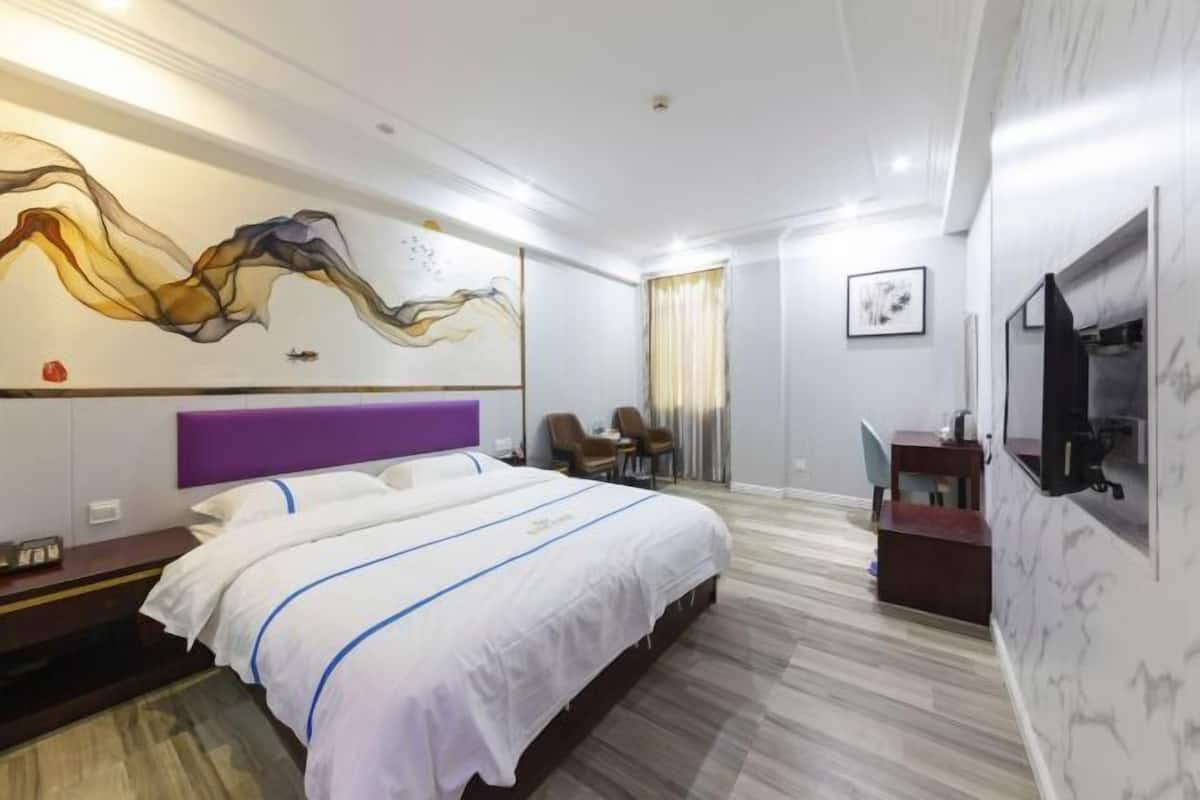 A hotel room with a bed, a desk, a chair, a TV, and a wall with abstract art.