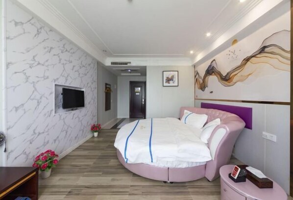 A modern bedroom with a round bed, marble-patterned walls, a flat-screen TV, and a decorative painting.