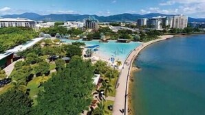 Un complex turístic a la costa amb piscina, vegetació i edificis al fons.