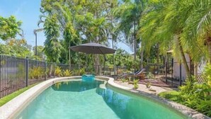 Une piscine à bord incurvé, entourée d’une clôture et d’une végétation luxuriante.