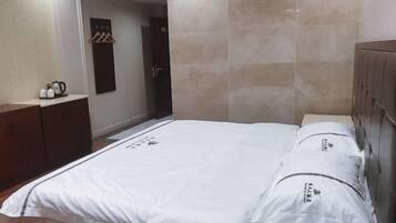 A hotel room with a bed, a wardrobe, and a small table with a kettle.