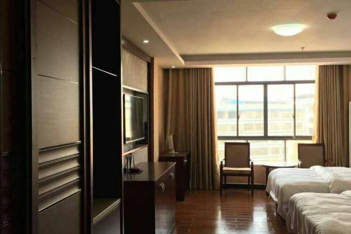 Quarto de hotel com uma cama, escrivaninha, cadeira, televisão e uma janela ampla.