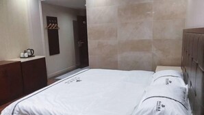 A hotel room with a bed, a wooden wardrobe, a small table with a kettle, and a wall-mounted towel rack. - Hengfeng Hotel (Qiyang)