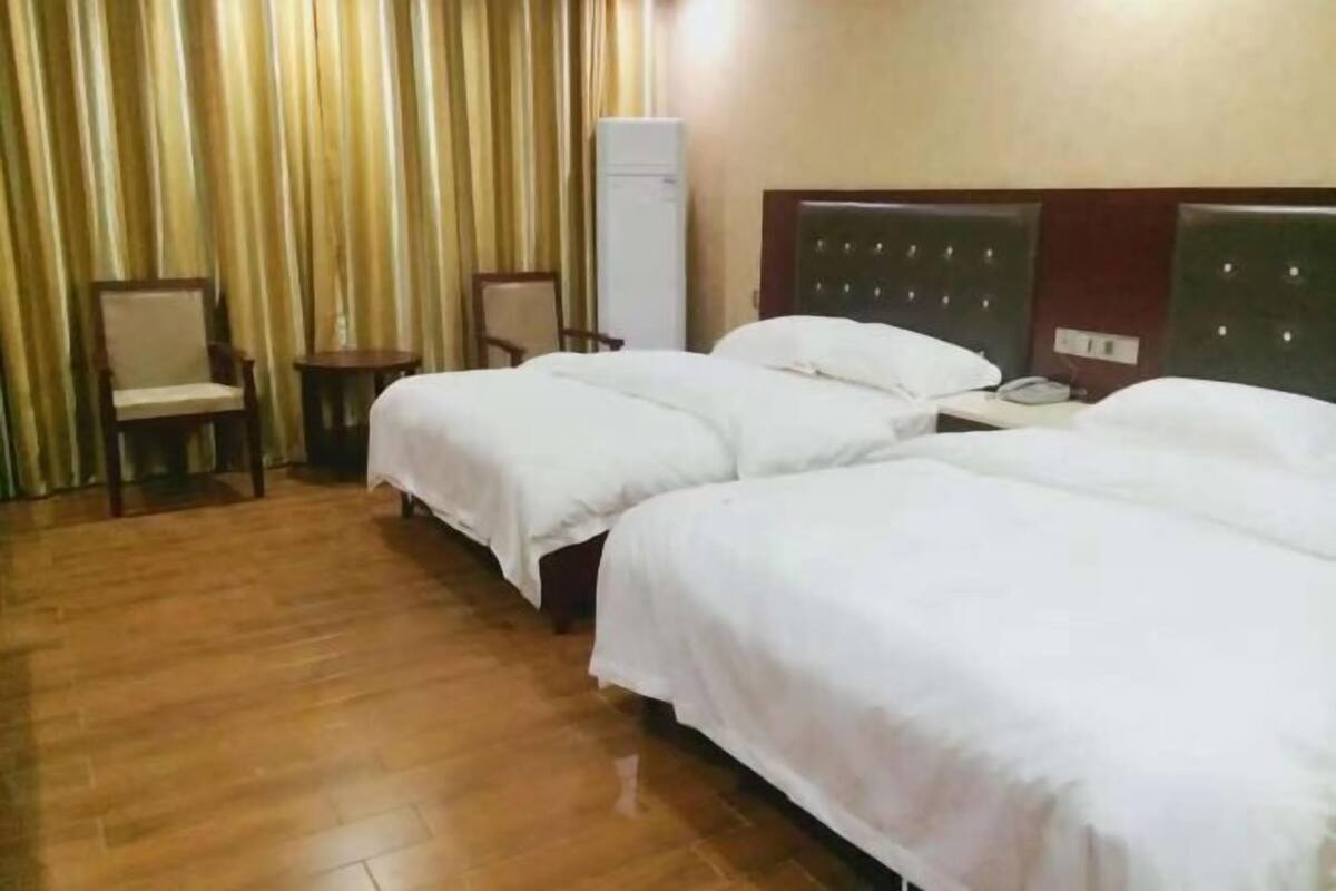 Quarto de hotel com duas camas, uma mesinha, uma cadeira e um aparelho de ar condicionado.