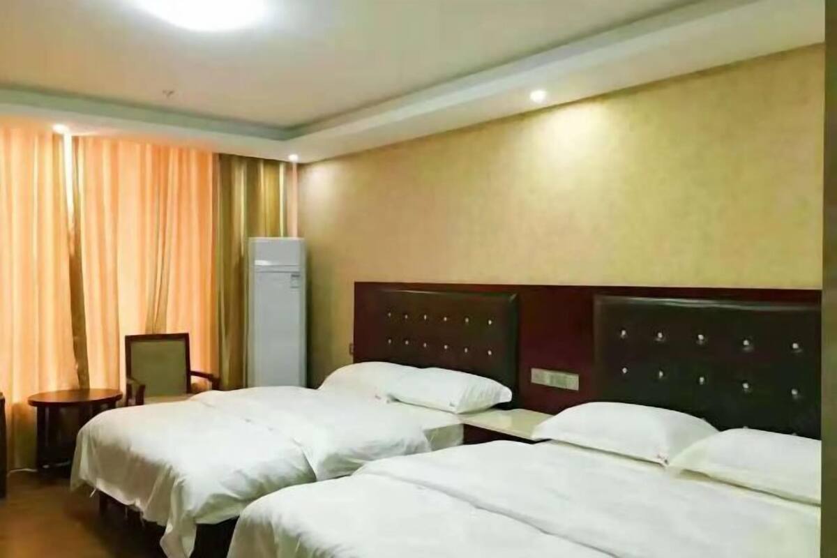 Quarto de hotel com duas camas, uma cadeira, uma mesinha e um frigorífico.