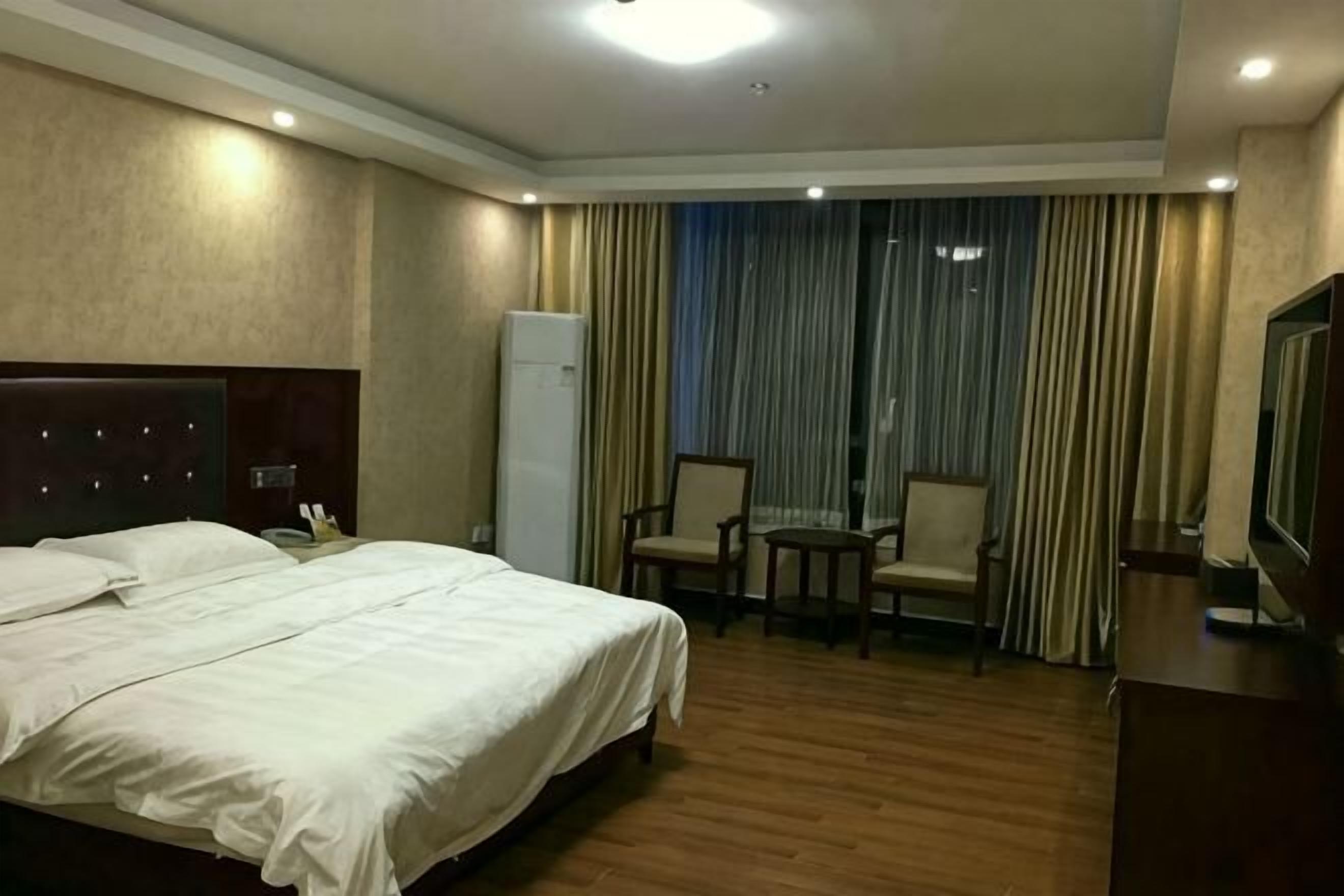 A hotel room with a large bed, a small table, two chairs, a television, and a refrigerator.