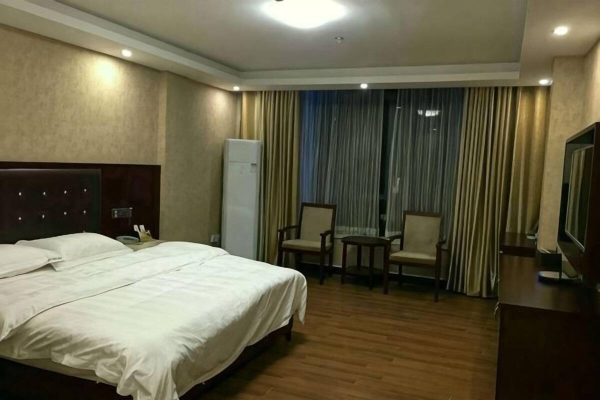 Quarto de hotel com uma cama grande, uma mesinha, duas cadeiras, uma televisão e um frigorífico.