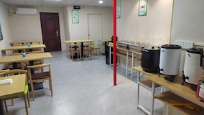 A classroom with wooden desks and chairs, a red pillar, and large water dispensers on a counter. - Nanning Haoyuan Business Hotel (Nanning)
