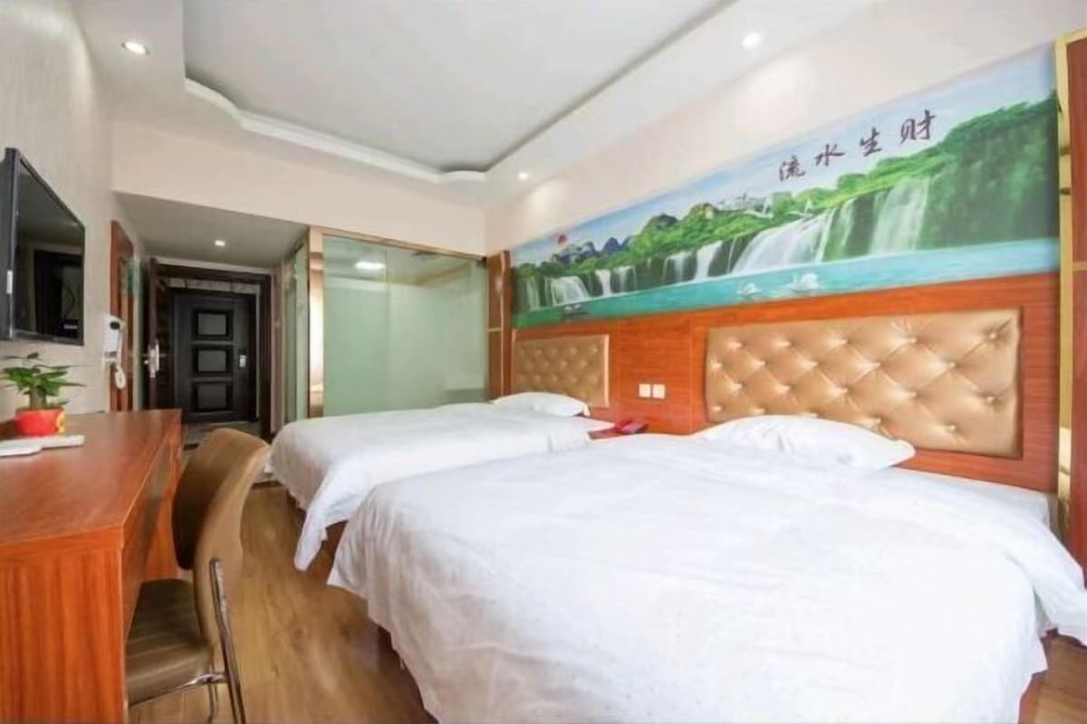 Habitación de hotel con dos camas, un escritorio de madera, una silla y un mural de una cascada.