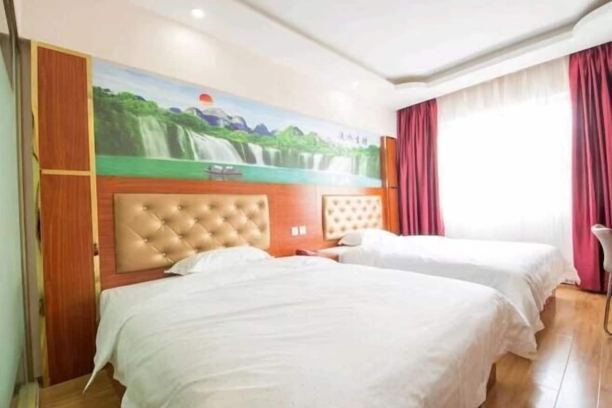 Ein Hotelzimmer mit zwei Betten, einem Wandgemälde eines Wasserfalls und roten Vorhängen.