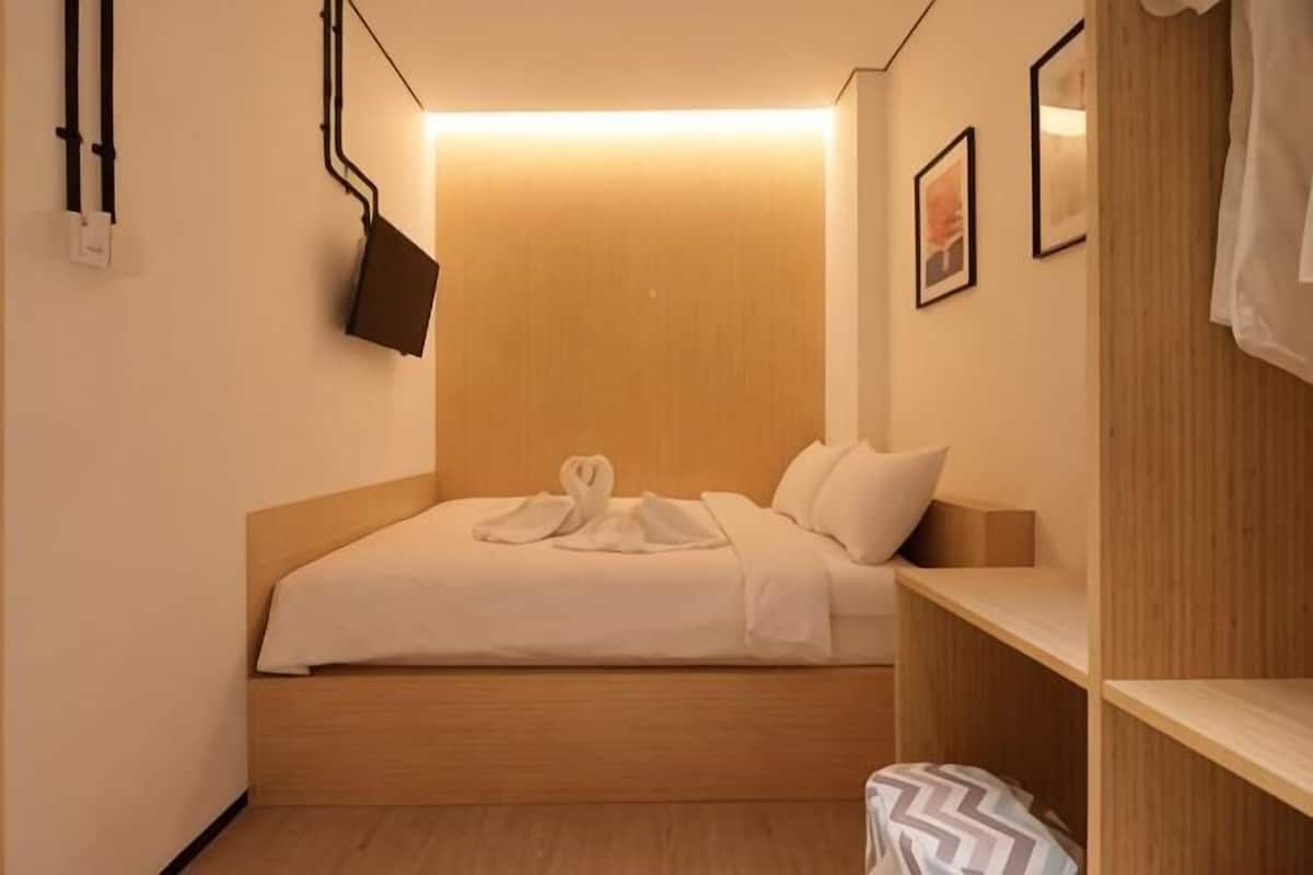 A hotel room with a wooden headboard, a bed with white linens, a bedside table, a wall-mounted TV, and a wardrobe.