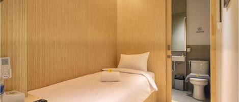A compact hotel room with a bed, bedside table, and a small desk with a remote control.