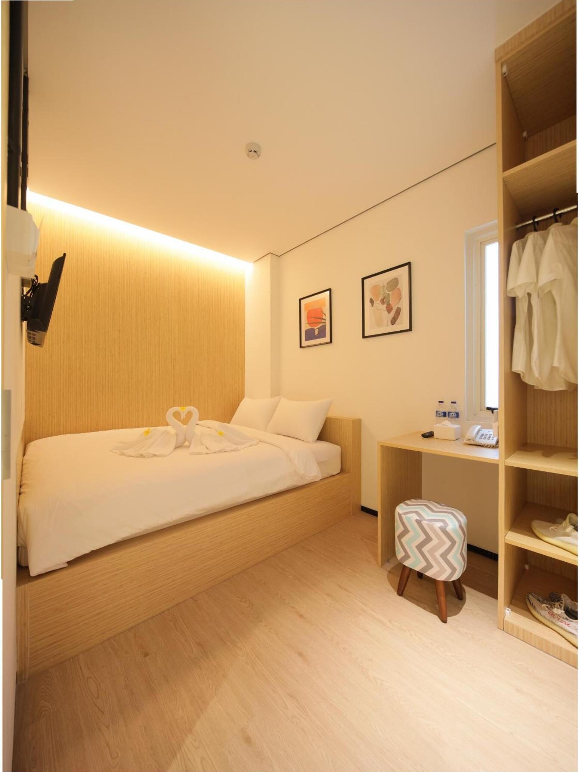 A hotel room with a bed, a desk, a chair, a wardrobe, and a wall-mounted light fixture.