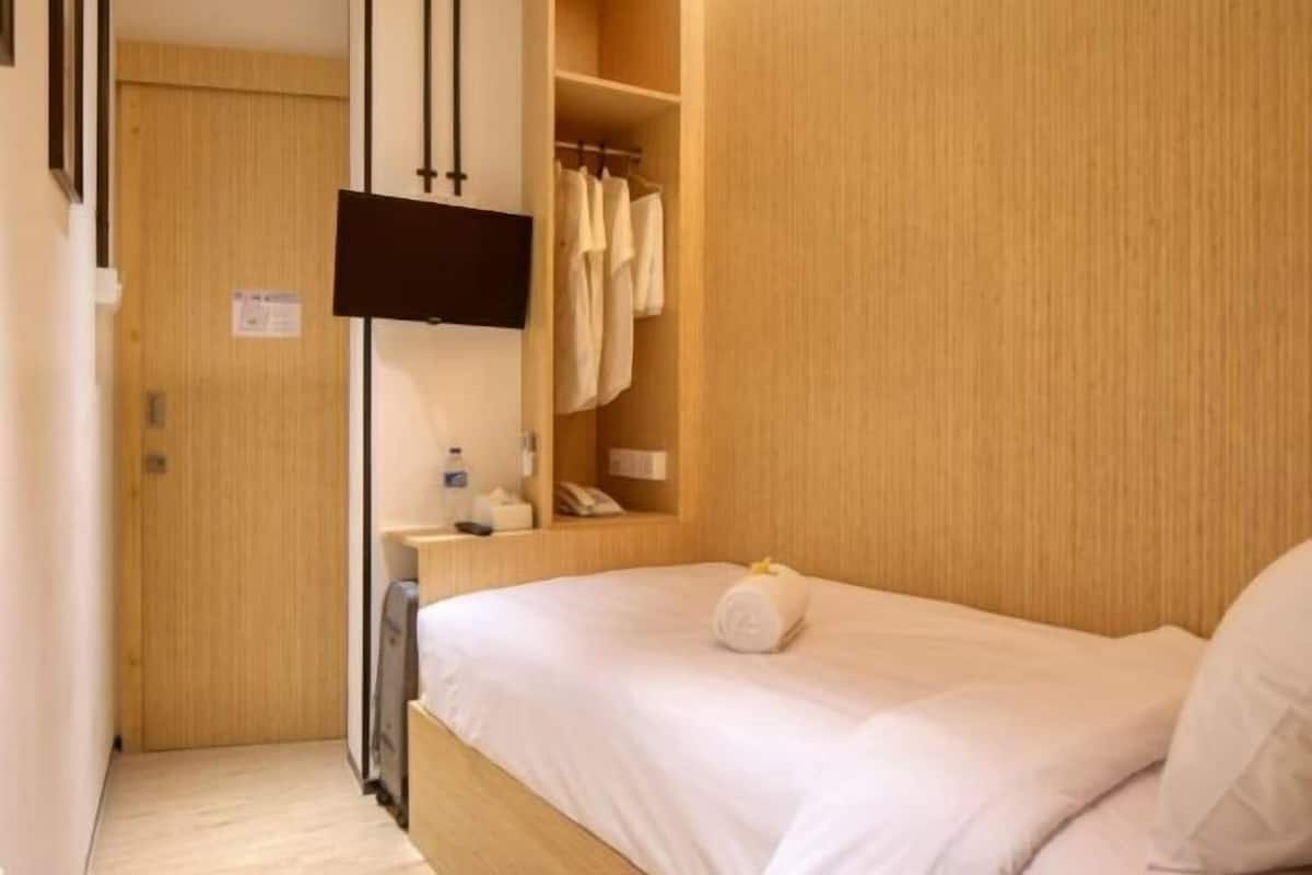 A hotel room with a bed, a wardrobe, a TV mounted on the wall, and a small table with a lamp.