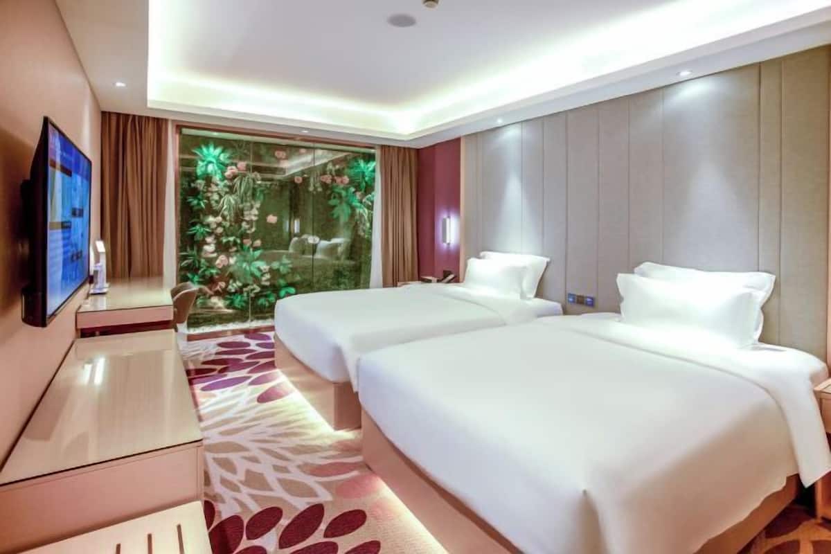 A hotel room with two beds, a TV, a glass door leading to a garden, and a patterned carpet.