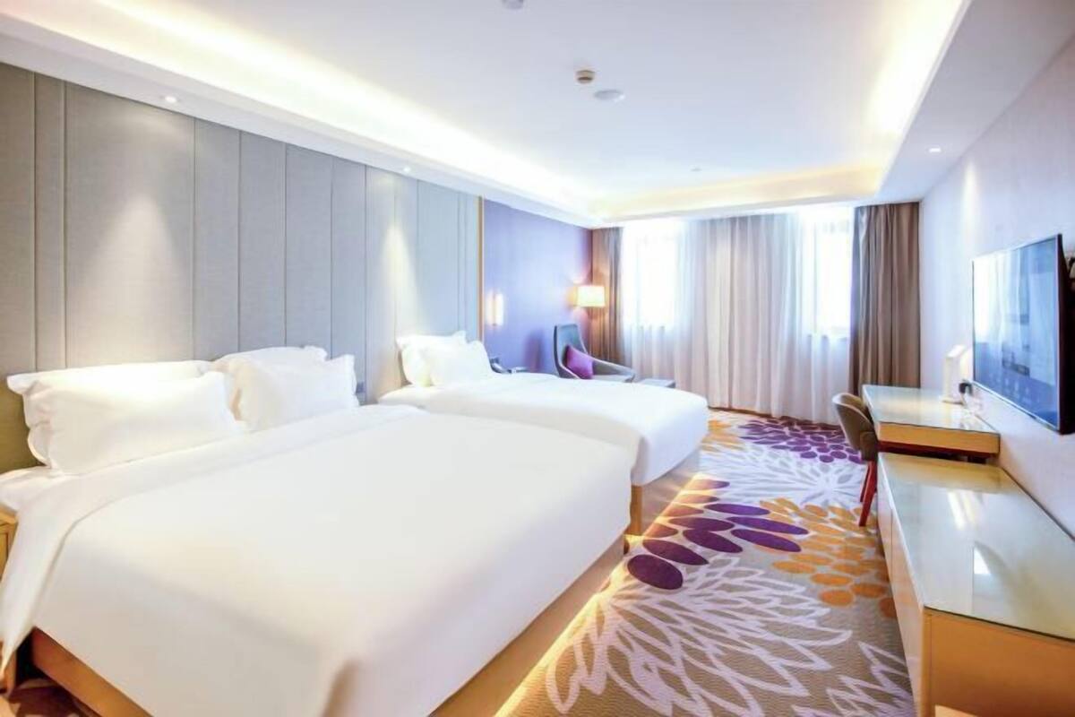 A hotel room with two beds, a desk, a chair, a TV, and a patterned carpet.