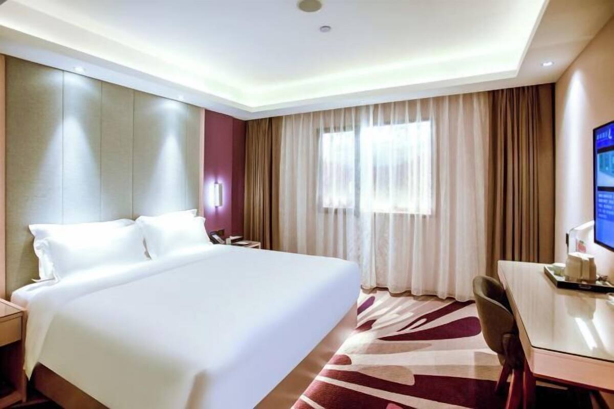 A hotel room with a large bed, a desk, a chair, and a television on the wall.