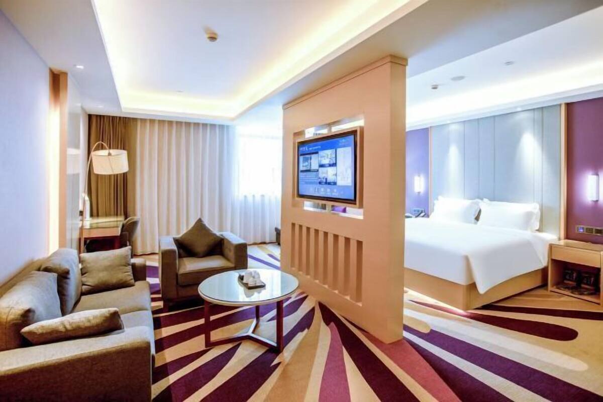 A hotel room with a bed, a sofa, a TV, and a small table.