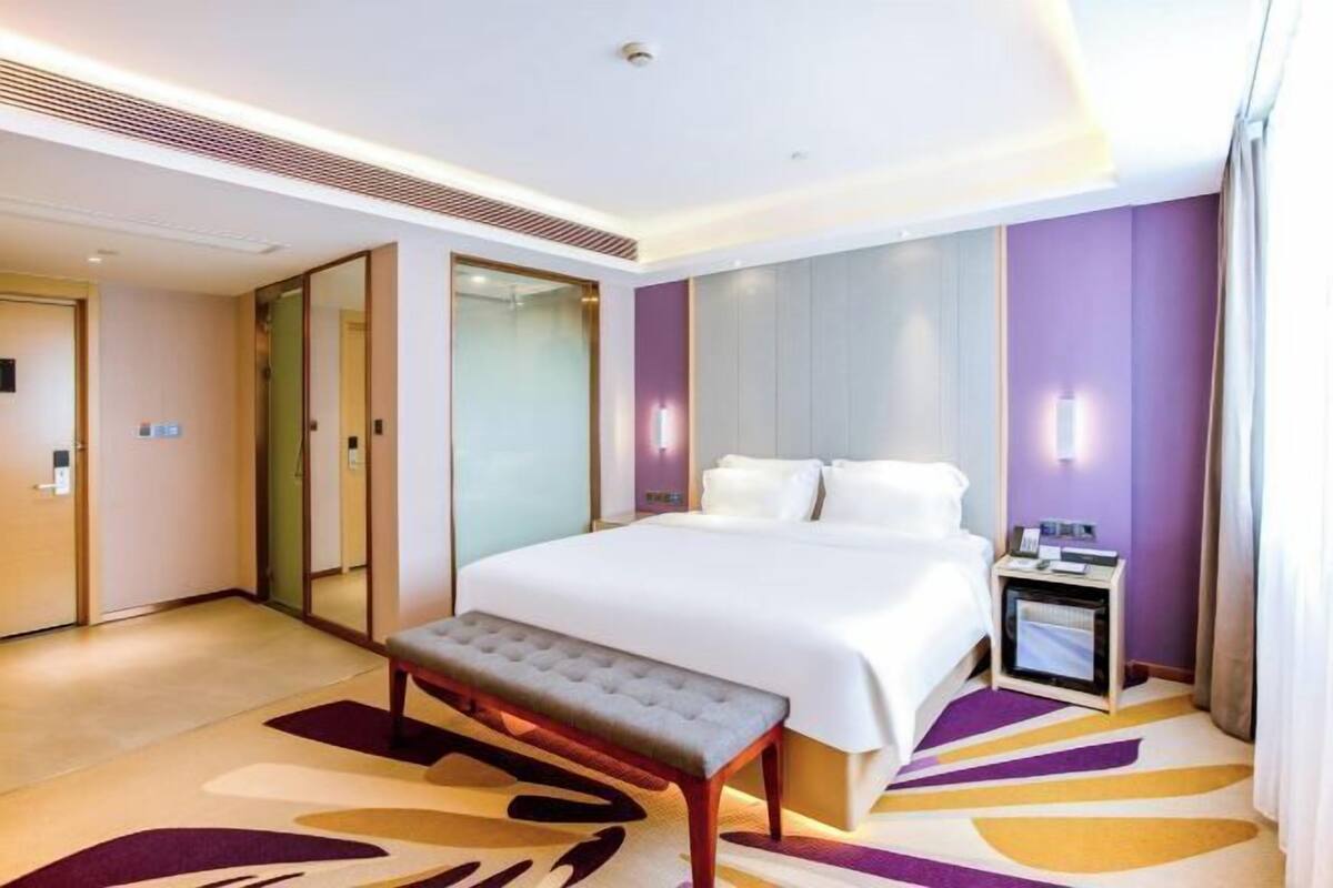 A hotel room with a large bed, a bench, a bedside table with a lamp, and a modern design.