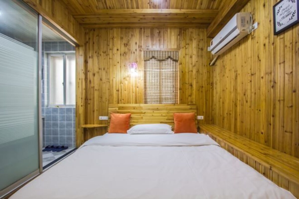 A wooden-paneled room with a bed, a window with blinds, and an air conditioning unit.