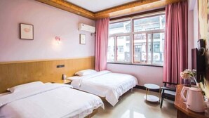 Ein Hotelzimmer mit zwei Betten, einer Holzbalkendecke, einem Fenster mit rosa Vorhängen, einem kleinen Tisch mit Wasserkocher und einem an der Wand befestigten Fernseher.