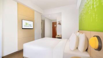 Een hotelkamer met een bed, een tv aan de muur, een telefoon en een groene wanddecoratie.