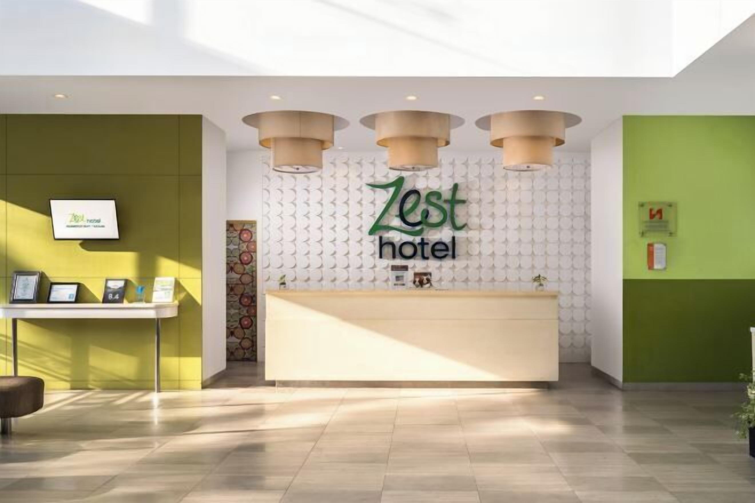 Een receptiegedeelte met een 'Zest Hotel' bord, een receptiebalie en een aan de muur bevestigde televisie.