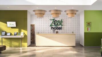 Een receptiegedeelte met een 'Zest Hotel' bord, een receptiebalie en een aan de muur bevestigde televisie.